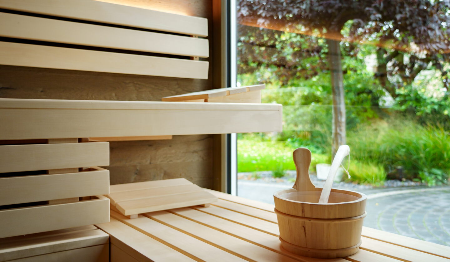 Saunabänke mit Kopfstützen und Aufgusskübel mit Saunakelle vor Panoramafenster